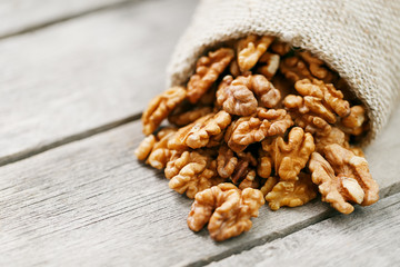 Walnuts in a burlap bag on a wooden gray background.