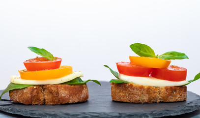 Two bruschetta Caprese on round shale board on white background with copy space. Vitamins against virus concept. Healthy food during quarantine. 