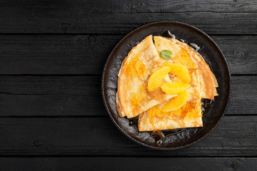 Crepes suzette - pancakes with orange sauce on black wooden table.