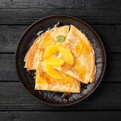 Crepes suzette - pancakes with orange sauce on black wooden table.
