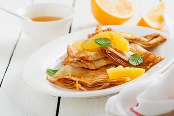 Crepes suzette - pancakes with orange sauce on white wooden table.