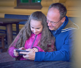 Middle-aged caucasian man looks with his granddaughter at family selfie in the phone