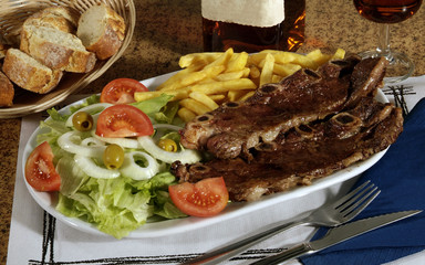 Plato combinado en una bandeja, con dos tiras de costilla de ternera a la brasa, patatas fritas y ensalada