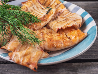 Grilled squid on a striped plate and a sprig of dill on an old wooden table.
