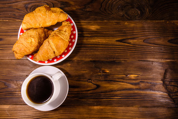 Cup of dark coffee and croissants on wooden table. Top view