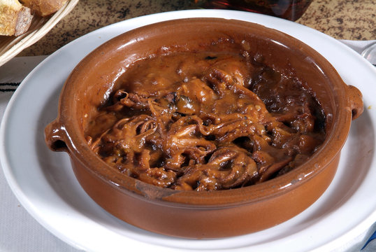 Tapas de pulpo en una cazuela, con salsa de tomate y cebolla.