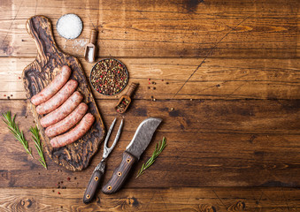 Raw beef and pork sausage on old chopping board with vintage knife and fork on wooden background.Salt and pepper with rosemary.Space for text