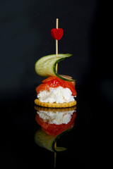 Beautifully designed canape of fresh goat cheese, cucumber slice and salmon with heart on dark background. Birthday, corporate or Valentine's day