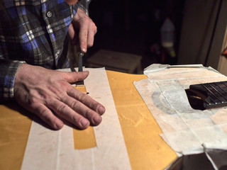 Installing a bridge on classical guitar body. The specialist removes varnish from the body of the...