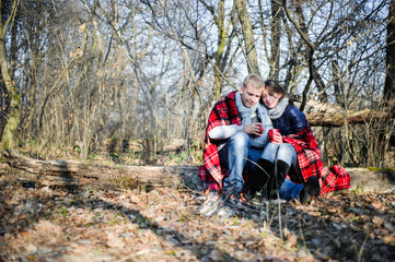 Pretty young couple relaxing near bonfire in the forest at evening time