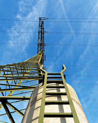 View from below up to a high voltage pylon, which stands on a concrete foundation, a ladder leads...
