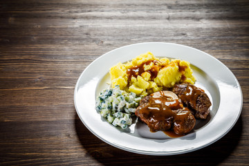 Grilled steak boiled potatoes and vegetable salad on wooden background