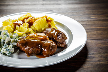Grilled steak boiled potatoes and vegetable salad on wooden background