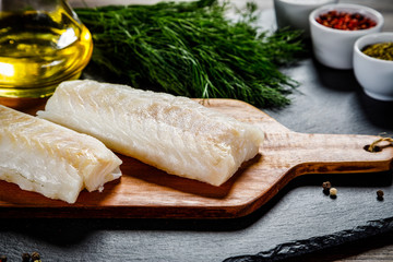 Fresh raw cod with herbs served on black stone on wooden table