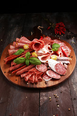 Food tray with delicious salami, pieces of sliced prosciutto crudo, sausage and basil. Meat platter with selection