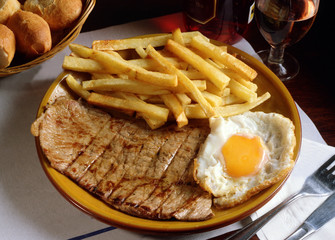 Plato de un bistec a la parrilla con un huevo y papas fritas