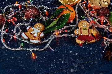 Lovely Christmas decoration close-up. New Year's things and sweets on a black wooden table. The gingerbread man keeps a cola of chewing marmalade.