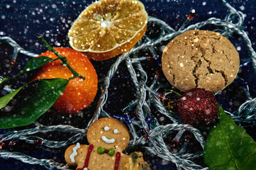 A bright Christmas card for congratulations. gingerbread man with a cheerful smile peeps out. Christmas garland with lights glows. Fresh and dried citrus, oatmeal cookies in the background.