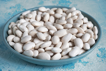White beans on a plate on a blue table.
