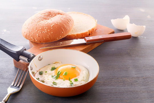 Fried egg in a pan and sliced bread cooked for breakfast on a wooden board. Copy space