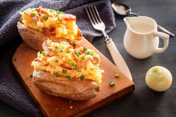 Baked potatoes with bacon and mushrooms in a rustic way on a wooden board. Close-up.
