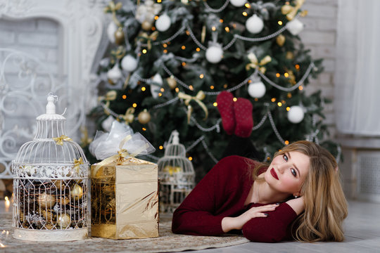 Happy young lady with long hair gifts by the fireplace near the Christmas tree