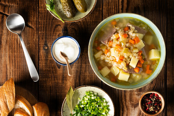 Rassolnik - Traditional Russian soup with pickled cucmbers, pearl barley, meat, pickles, carrots and potatoes on a dark wooden background. Top view