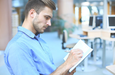 Portrait of handsome smiling man in casual shirt taking notes at workplace.