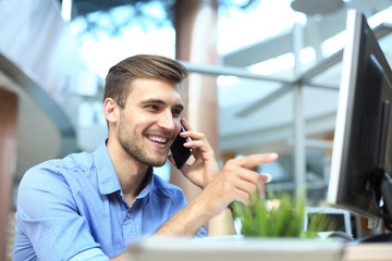Smiling businessman sitting and using mobile phone in office.