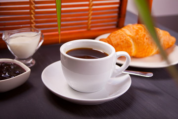 Cup of coffee with fresh croissant, honey and jam on the table.