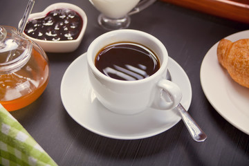 Cup of coffee with fresh croissant, honey and jam on the table.
