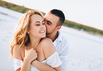 A bearded man and a blond woman hugging against the background of white sand. Portrait of emotional people at sunset. Love in the desert newlyweds. The love story of merry and lovers young.