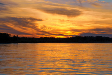 Obraz premium Beautiful sunset on the river. Summer sunset or sunrise landscape with golden light in Yakutia, Republic of Sakha, Russia. Riverscape taken from a ferry on river Lena