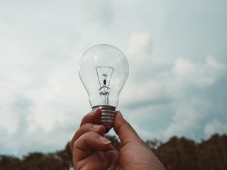 Concept save energy efficiency. Hand holding light bulb on blurred tree and sky background