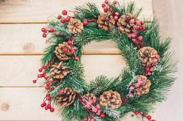 Christmas wreath of fir branches with cones, snow, red berries on a wooden background