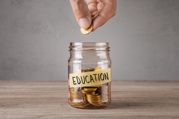 Education. Glass jar with coins and an inscription education. Man holds  coin in his hand