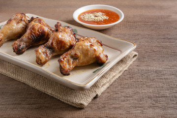 grilled chicken drumette in a ceramic plate served with spicy sauce on wooden table. homemade style food concept.
