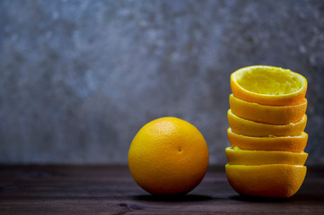 A composition of halves of orange peel and one orange on a wooden table on a gray background. Fresh...
