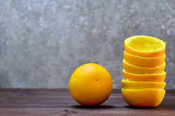 A composition of halves of orange peel and one orange on a wooden table on a gray background. Fresh...