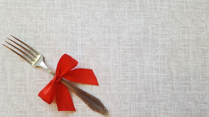 A fork with a red bow lies on the tablecloth. A place to record. Photo for the menu of cafe, restaurant, dining room, pizzeria. A place for a festive menu.