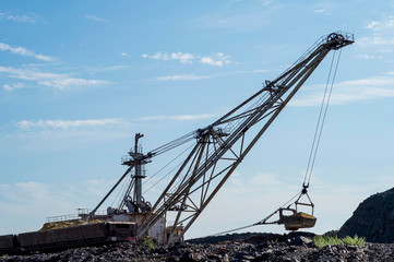 A huge excavator overloads in the dumps rock from the unloaded train from the mine against a clear blue sky. Concept: mining and environmental problems