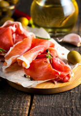 Closeup of thin slices of prosciutto with mixed olives and paprika on wooden cutting board
