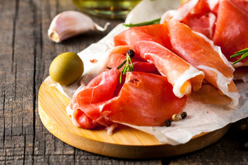 Closeup of thin slices of prosciutto with mixed olives and paprika on wooden cutting board