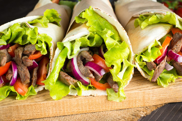 Photo of Mexican sandwich food, burrito, fajita, tacos, wrap made of tortilla, beef, chicken, fresh vegetables on rustic wooden background. Fast food concept. Healthy lunch snack. Copy space. 