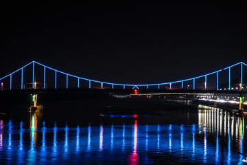 Night european city in blue and red lights and reflection in water, Kyiv (Kiev) the capital of Ukraine. Pedestrian bridge across the Dnieper river and view from the river station, evening illumination