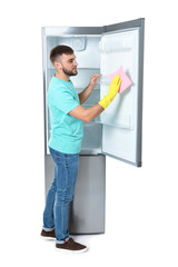 Young man cleaning refrigerator with rag on white background
