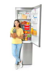Fototapeta na wymiar Young woman with pineapple near open refrigerator on white background