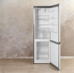 Open refrigerator with empty shelves near grey wall indoors. Space for text