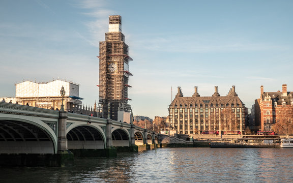 A view over the River Thames towards the bridge and Palace of Westminster with the Big Ben clock tower covered in scaffolding during renovation work.