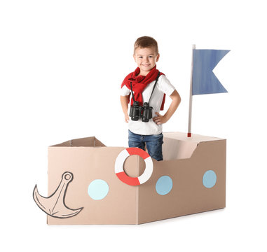 Cute little boy playing with cardboard ship on white background